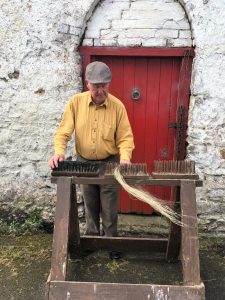 ‘Hackling’ This is the final step in dressing the flax. The fibres are split and straightened by being drawn through a graded series of combs or ‘hackles’ The long fibres are used for weaving and the shorter coarser fibres which catch on the comb (called ‘tow’) can be used to make rougher cloth. The woody waste matter, known locally as ‘shous’ was often used as firewood. Courtesy Fred Faulkener